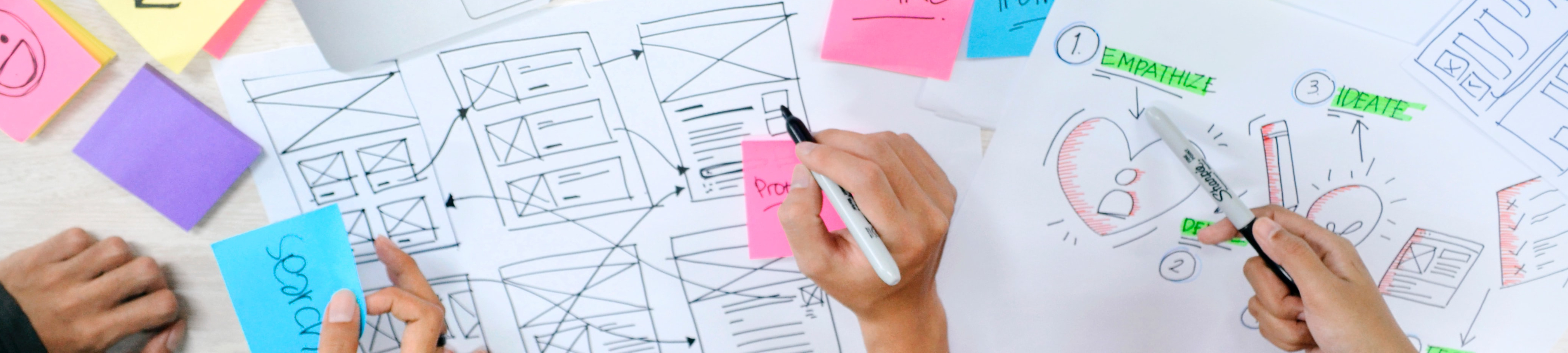 A photo of people writing on and placing sticky notes on a series of diagrams and sketches