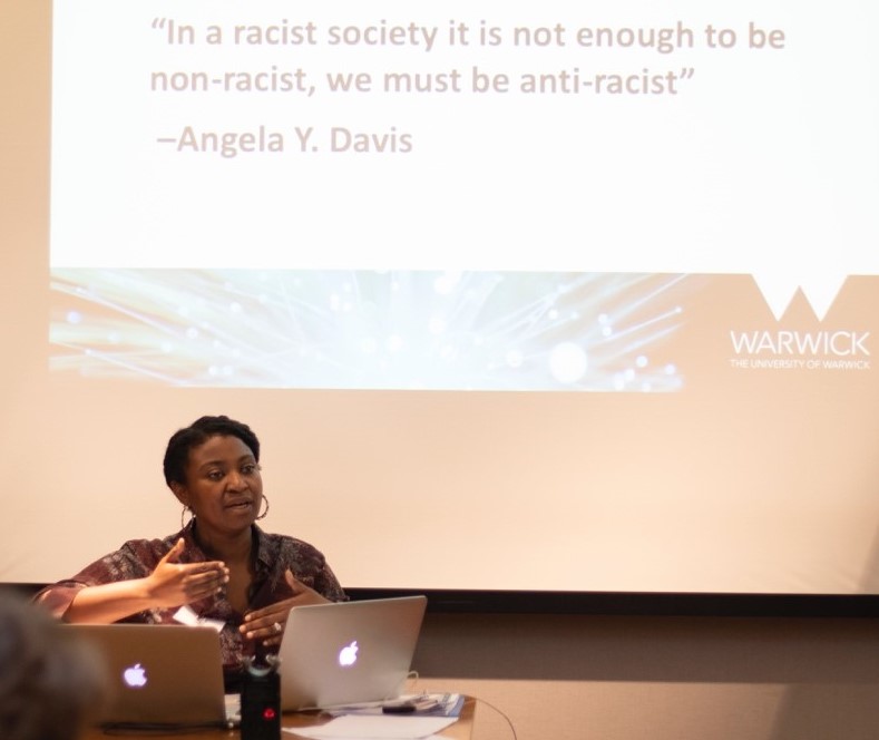 Keynote speaker Dr Meleisa Ono-George in front of a slide quoting Angela Y Davis - in a racist society it is not enough to be non-racist; we must be anti-racist