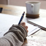 A person writing in a book at a table with coffee and papers