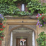 An arch in Selwyn College surrounded by ivy and hanging baskets full of flowers