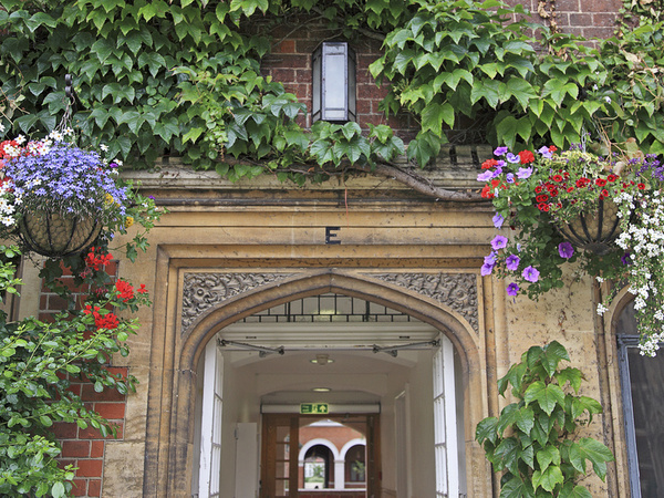 An arch in Selwyn College surrounded by ivy and hanging baskets full of flowers