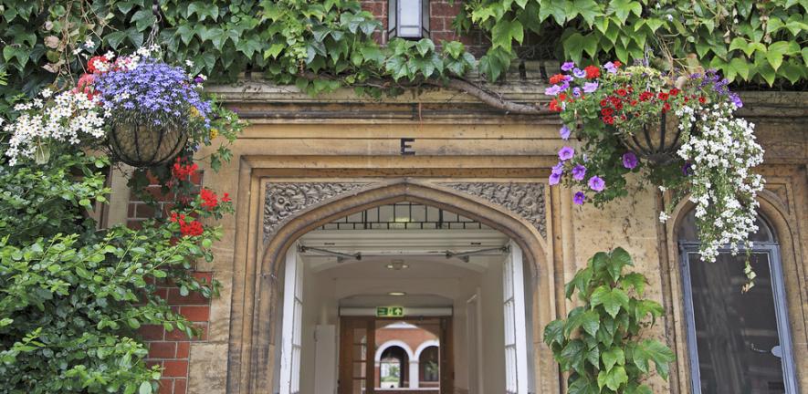 An arch in Selwyn College surrounded by ivy and hanging baskets full of flowers