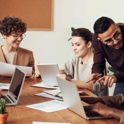 Group of people discussing work at a table with laptops