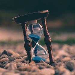 An hourglass resting on pebbles running out of sand