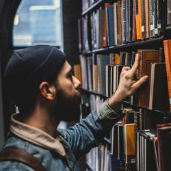 Man carrying a rucksack selecting a book from a library shelf