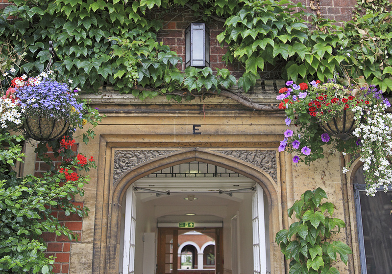 An arch in Selwyn College surrounded by ivy and hanging baskets full of flowers