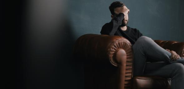 Man on sofa looking distressed with head in hand