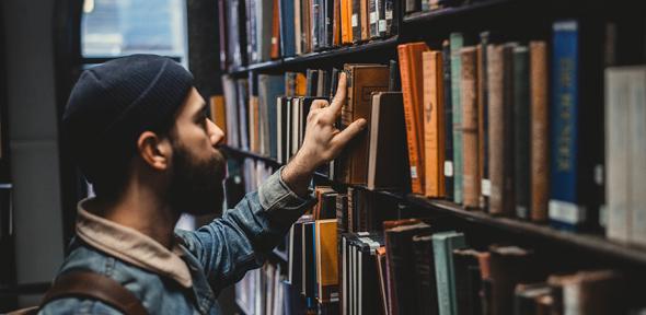 Man carrying a rucksack selecting a book from a library shelf