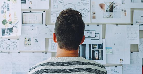 Man staring at a wall board covered in different notes and papers