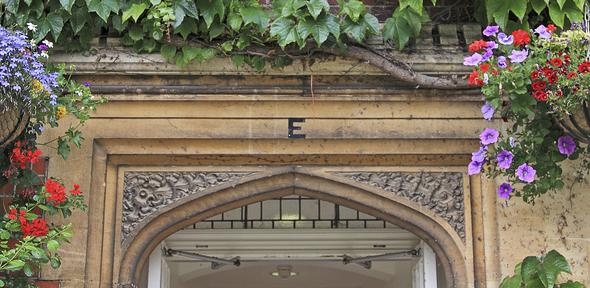 An arch in Selwyn College surrounded by ivy and hanging baskets full of flowers