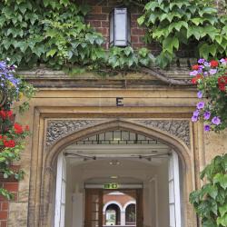 An arch in Selwyn College surrounded by ivy and hanging baskets full of flowers