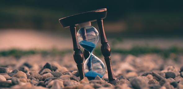 An hourglass resting on pebbles running out of sand