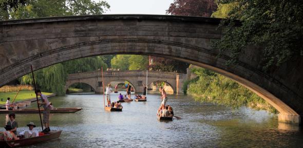 View along the river Cam dotted with punters beneath the arch of a bridge