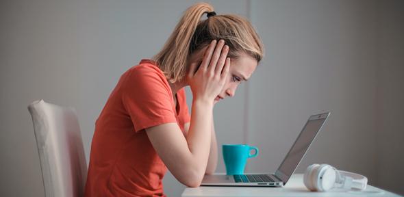 Woman with head in hands in front of a laptop